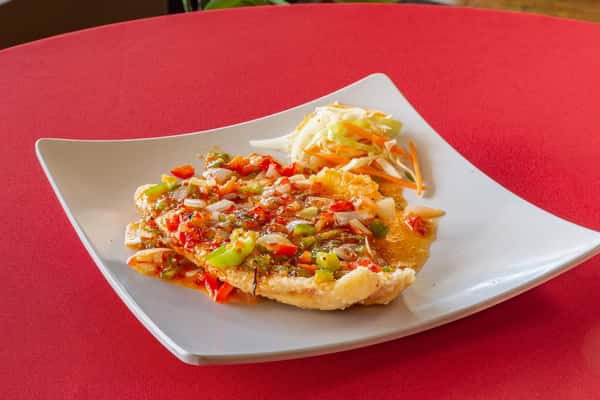 Crispy Thai-style omelet topped with sweet chili sauce, diced onions, and bell peppers, served with egg rolls in the background.