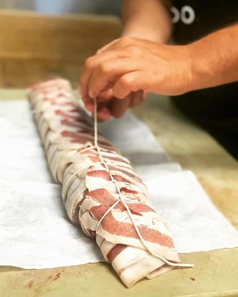 chef rolling bacon around meat