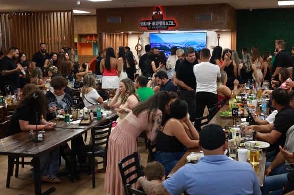 Lively evening crowd at Bonfire Brazil Steakhouse, with guests enjoying drinks and grilled meats in a vibrant, social dining atmosphere. The upscale churrascaria features long communal tables, a bustling bar scene, and a mix of families and friends celebrating together.