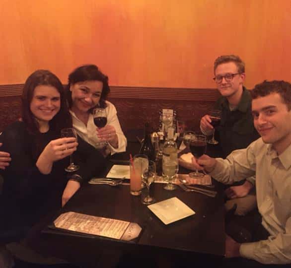 four customers smiling and holding up their glasses of red wine