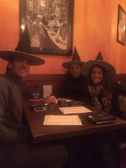 three customers smiling at a booth while wearing witch hats