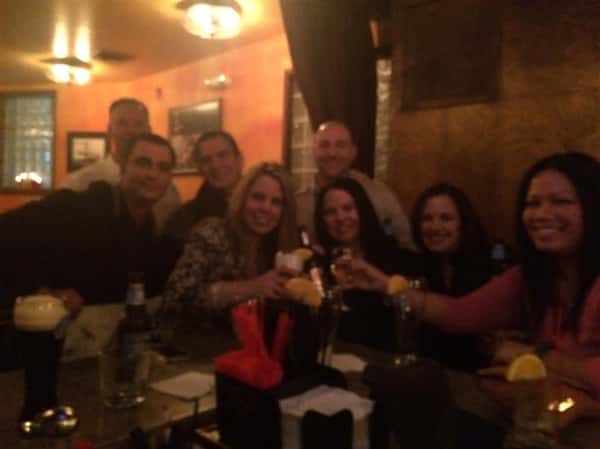 8 customers smiling and holding their drinks up around the bar