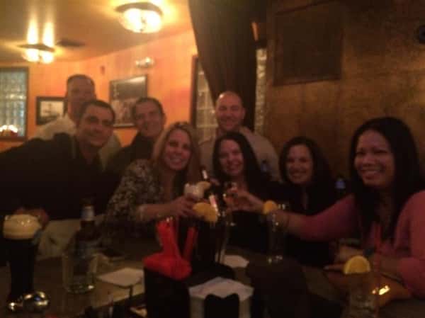 8 customers smiling and holding their drinks up around the bar