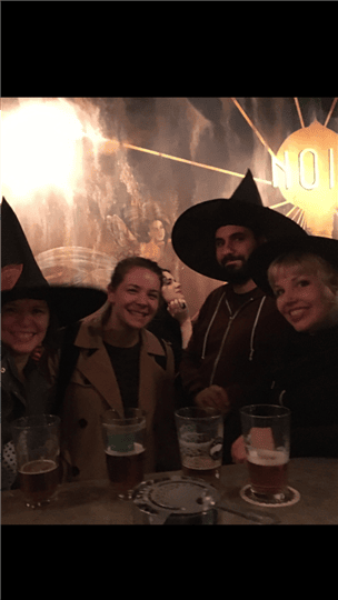 a group of four friends posing together while half of them wear witch hats