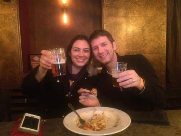 two friends holding up their beers and smiling with a plate of food