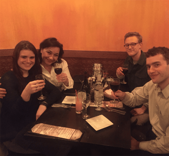four customers smiling and holding up their glasses of red wine