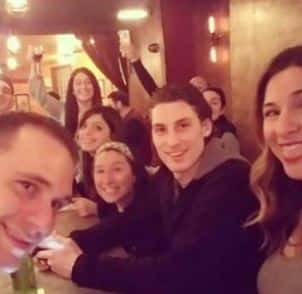 a big group of friends smiling and holding up their drinks