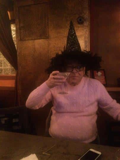 a customer holding up his martini while wearing a witch hat