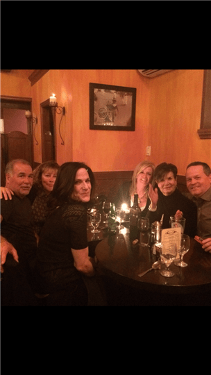 a group of six friends smiling together around a table