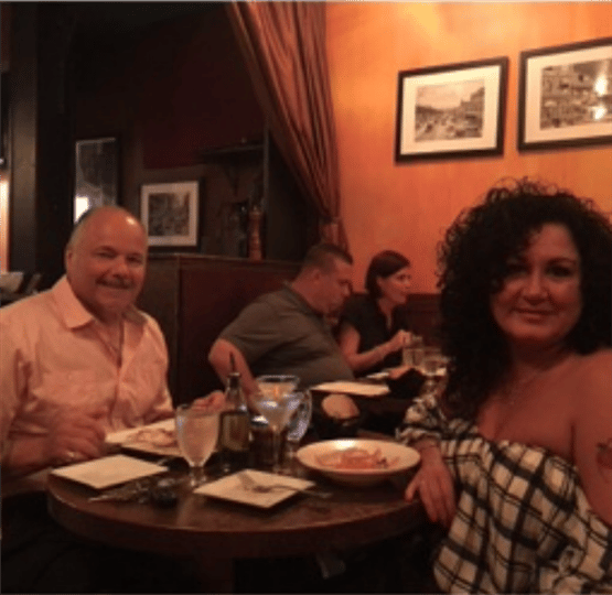 a couple smiling at their table with drinks and two plates of food
