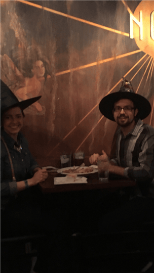 a couple smiling at their table while wearing witch hats