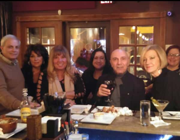 seven customers smiling at the bar area with food and drinks
