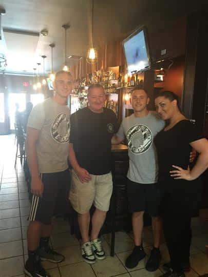 a group of four customers posing outside the bar