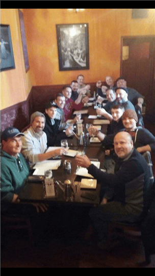 big group of people smiling and holding their drinks up around a table
