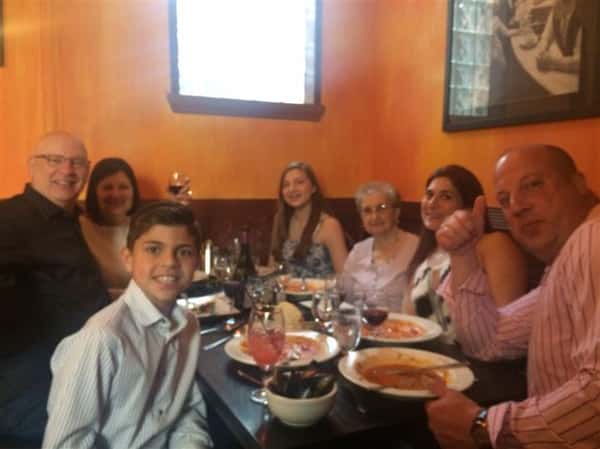 a group of 7 smiling together at their table with food and drinks