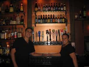 two bartenders smiling in front of a wall of liquor bottles