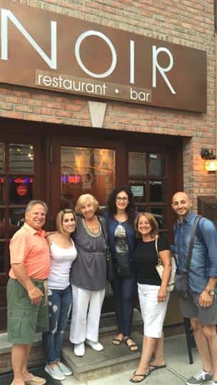 a group of six friends smiling and posing outside the front of the restaurant