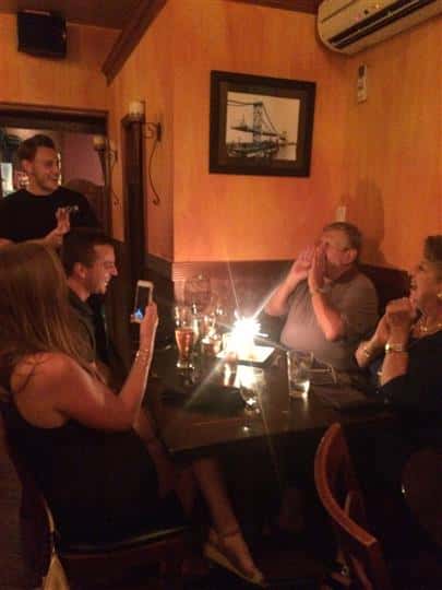 three customers singing happy birthday with their friend who is blowing out the candles