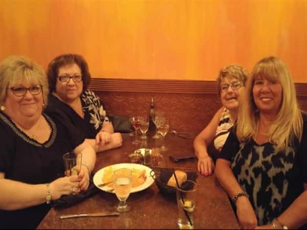 four customers smiling at their table with a plate of food
