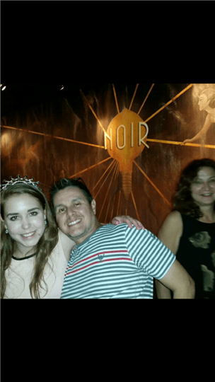 three customers posing outside the painting of a light bulb with the word "Noir" on it