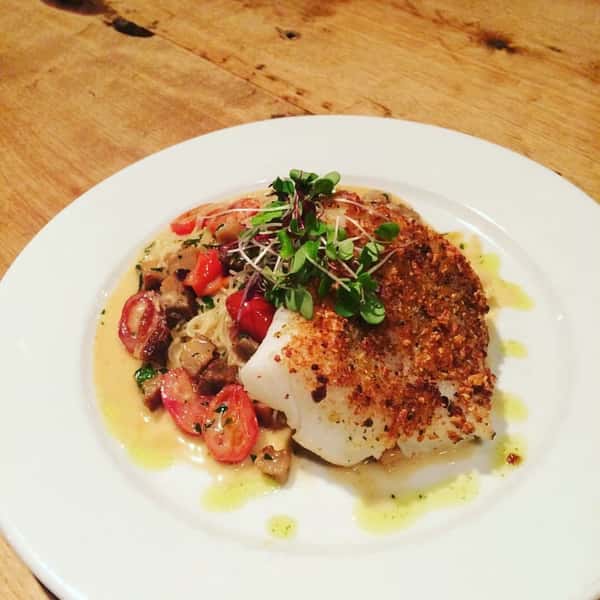 Fried cod over spaghetti topped with tomatoes and garnish