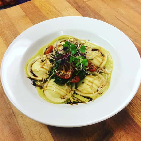 Ravioli's topped with tomatoes and garnish in a sauce in a bowl