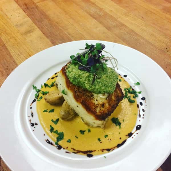 Seared Pork Chop topped with pesto and garnish on a plate with sauce