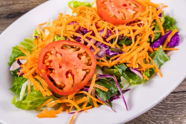 Fresh garden salad with crisp romaine lettuce, shredded carrots, red cabbage, sliced tomatoes, and mixed greens served on a white plate.