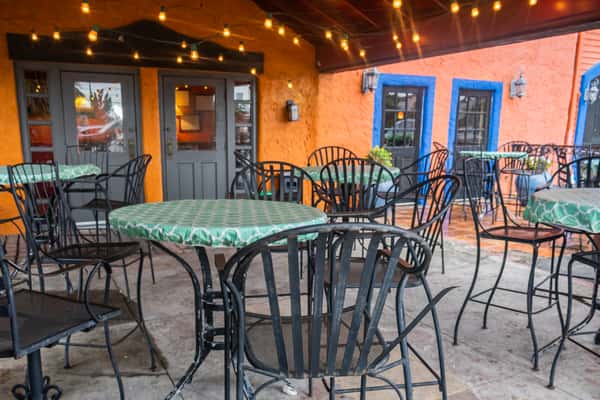 Covered outdoor restaurant patio with string lights, wrought-iron tables and chairs, and a warm, inviting atmosphere for casual dining and evening gatherings.