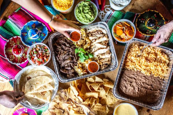 Family style Mexican feast featuring grilled meats, quesadillas, chips, beans, and fresh toppings.