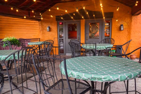 Covered outdoor restaurant patio with string lights, wrought-iron tables and chairs, and a cozy atmosphere for casual dining and evening gatherings.