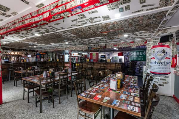 Indoor dining space with wooden tables, bar seating, and a ceiling covered in signed dollar bills, reflecting Cherry Pocket's quirky, laid-back vibe.