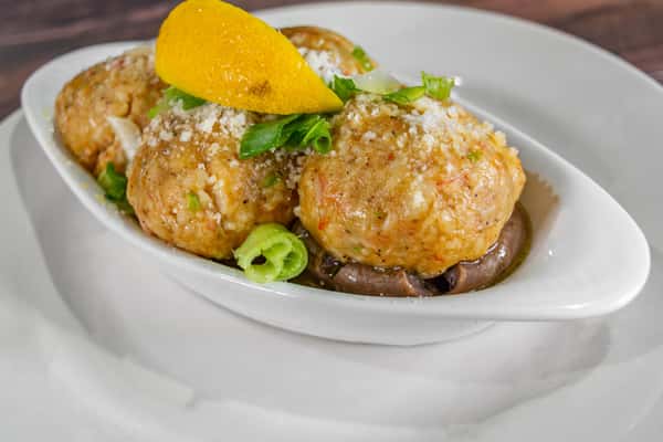 Baked seafood stuffing balls garnished with scallions and Parmesan cheese, served in a shallow white dish with mushrooms and a lemon wedge for garnish.