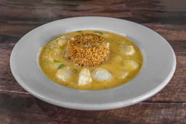 Bowl of creamy seafood stew with tender white fish and a mound of seasoned rice in the center, served in a rich, golden broth on a white plate.