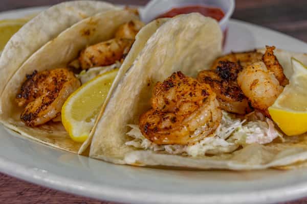 Close-up of grilled shrimp tacos with shredded slaw on soft flour tortillas, garnished with fresh lemon wedges and served with a side of salsa, highlighting a coastal seafood dish perfect for a beachside restaurant menu.