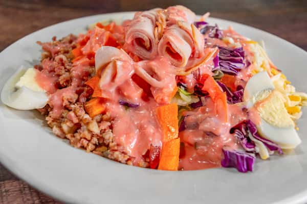 Colorful chopped salad topped with creamy pink dressing, rolled deli meat, bacon crumbles, sliced egg, and shredded carrots for a hearty, fresh starter.