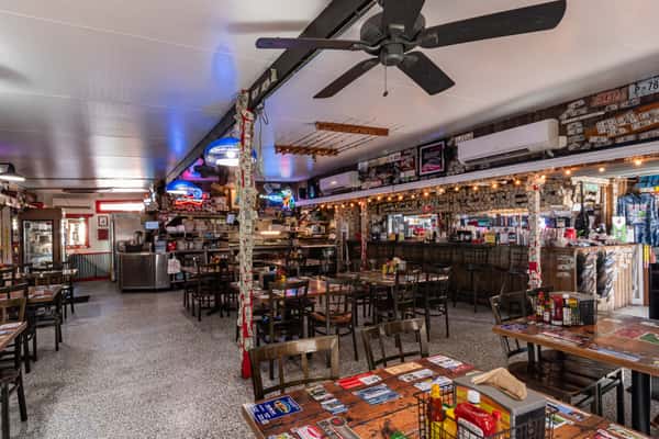 Eclectic bar and dining space with neon beer signs, dollar bill-covered walls, and rustic wood furnishings, capturing the quirky charm of Cherry Pocket's casual seafood joint.
