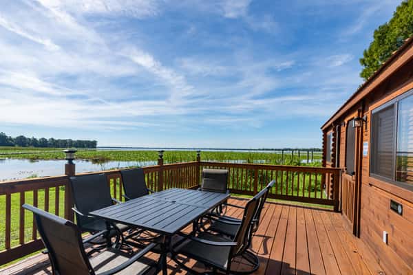 Scenic lakefront cabin deck with a black patio dining set overlooking tranquil waters and marsh grasses, offering peaceful outdoor seating at a Florida lakeside retreat.