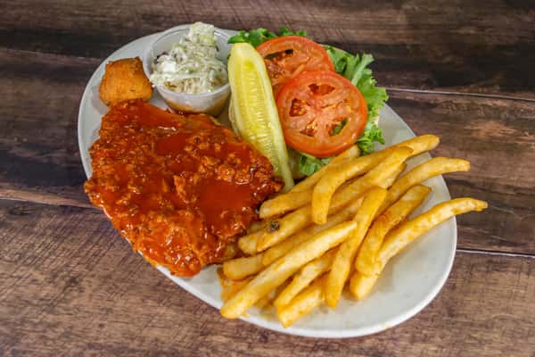 Close-up of a spicy buffalo chicken sandwich platter with seasoned fries, coleslaw, hush puppy, and fresh veggies on a rustic wooden table.
