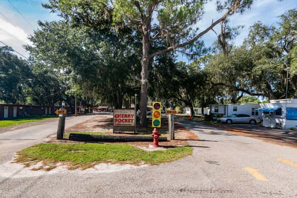 Rustic entrance to Cherry Pocket featuring a red-and-yellow traffic light, log posts, and a welcome sign, surrounded by trees and RVs.