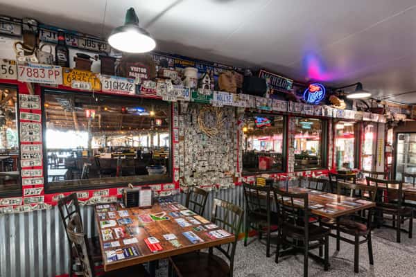 Quirky dining corner at Cherry Pocket with corrugated metal paneling, dollar bills and license plates decorating the walls, and tables covered in beer-branded designs.