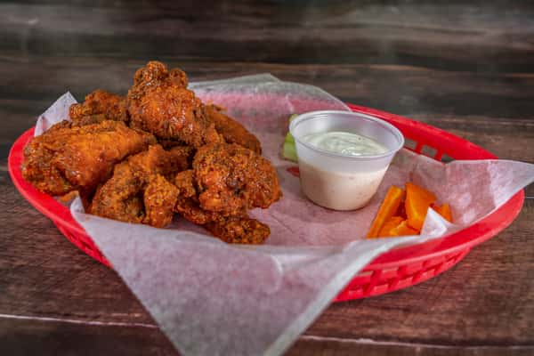 Crispy fried chicken wings served in a red basket with ranch dressing, celery, and carrot sticks for a classic bar-style appetizer.