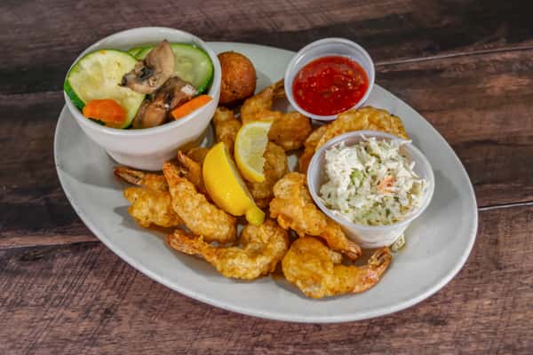 Crispy fried shrimp served with creamy coleslaw, sautéed mixed vegetables, cocktail sauce, and a hush puppy, presented on a white plate as a classic coastal seafood combo.