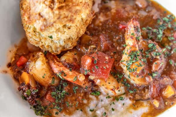 Piping hot shrimp rest on top of grits, accompanied by a fresh house biscuit.