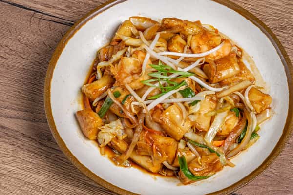 Stir-fried flat rice noodles with shrimp, tofu, bean sprouts, cabbage, and scallions in a savory brown sauce.