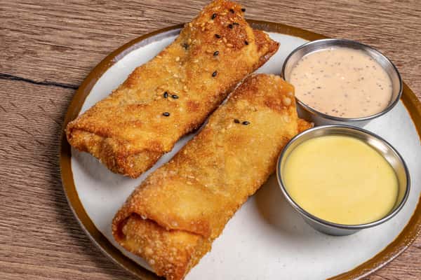 Two crispy sesame-coated egg rolls served with creamy pepper and honey mustard dipping sauces on a ceramic plate.