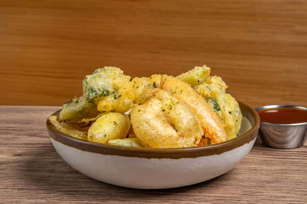Assorted vegetable tempura including broccoli, carrots, and squash, served in a bowl with dipping sauce on the side.