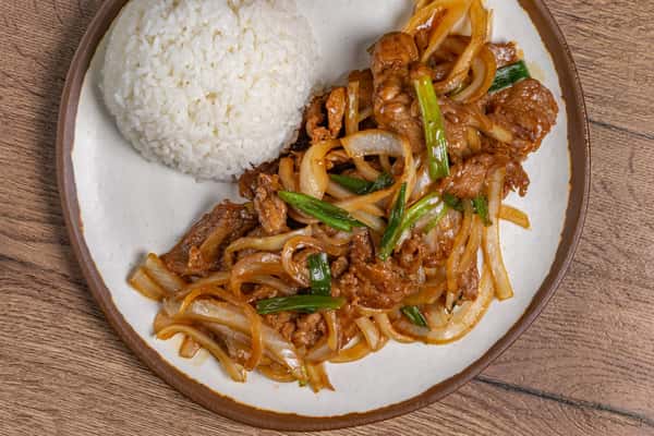 Beef stir-fry with onions and scallions in a savory sauce, served with a mound of steamed white rice.