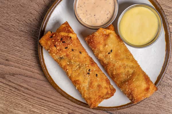 Two crispy sesame-coated egg rolls served with creamy pepper and honey mustard dipping sauces on a ceramic plate.