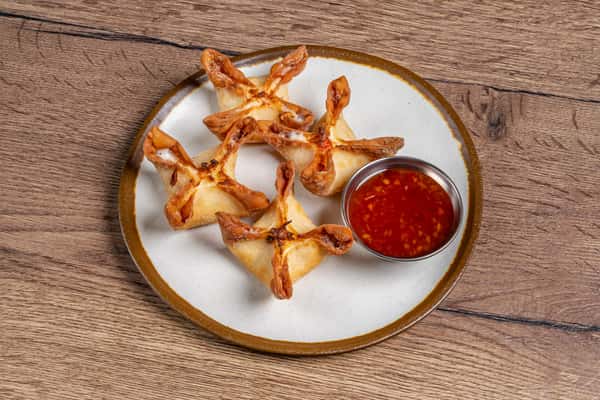 Golden crab rangoon served on a plate with a side of sweet chili dipping sauce.